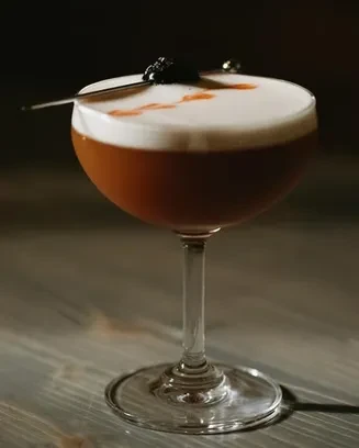 Amber cocktail in coupe glass with foam, red streaks, and cherry.