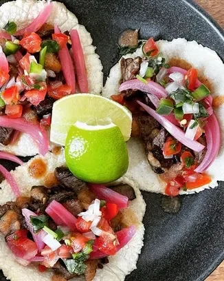 Overhead: Three tacos with meat, salsa, pickled onions, and lime.