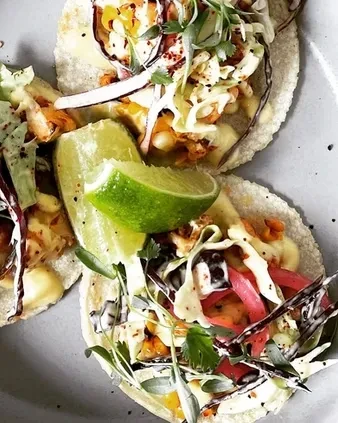 Three soft tacos filled with protein, slaw, pickled onions, and lime.