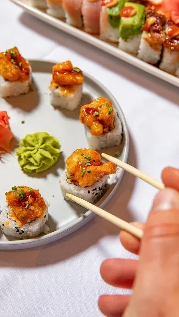 Hand picking a sushi roll with orange topping, wasabi, and ginger.