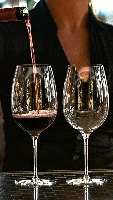 Red wine is poured from bottle into a stemmed glass.