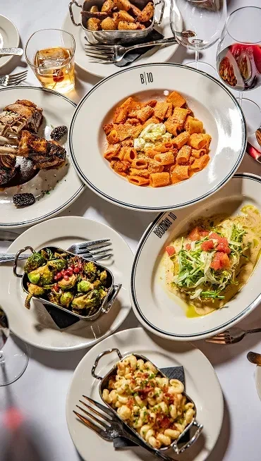 Overhead view of diverse restaurant dishes and drinks on a white tablecloth.