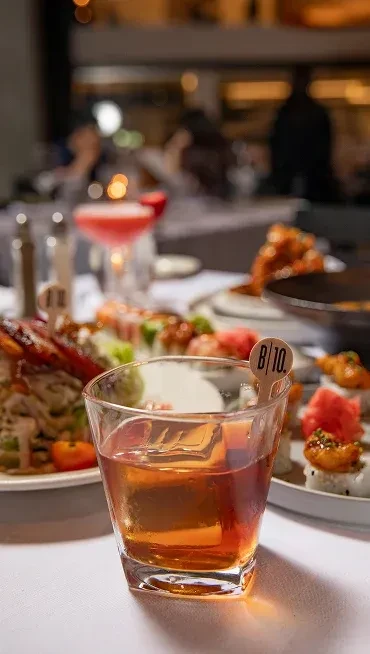 Amber cocktail, sushi, and plates of food in a blurred restaurant.