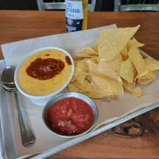 Queso, salsa, and tortilla chips on a metal tray with Corona beer.