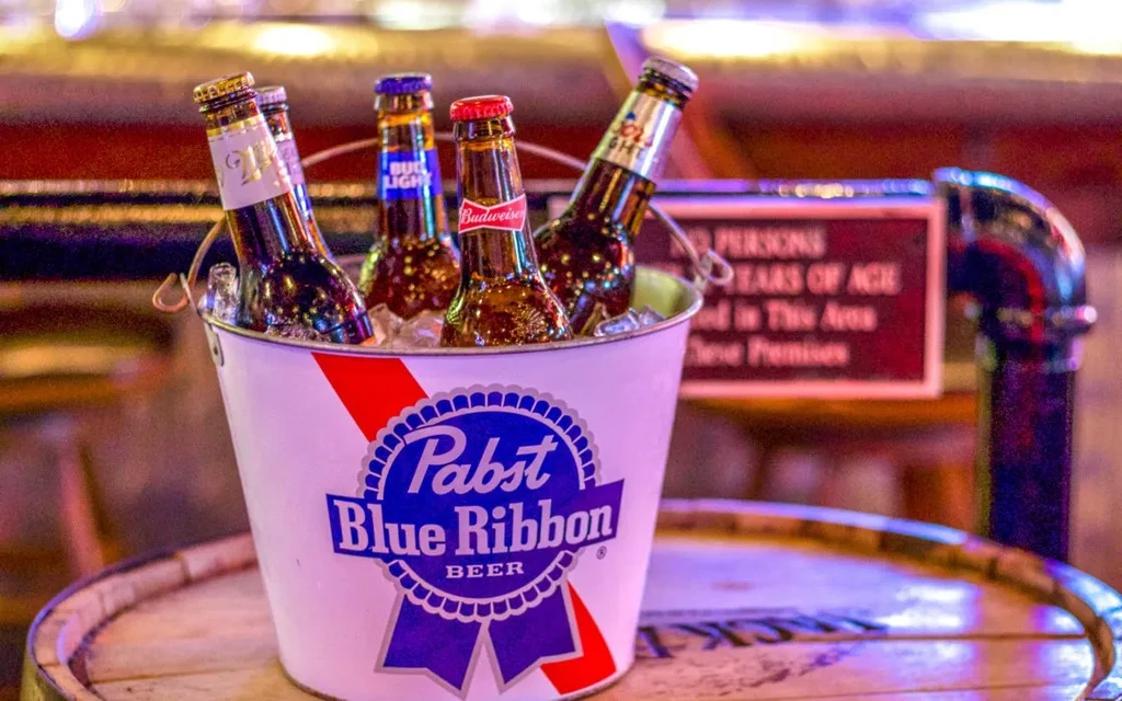 Pabst Blue Ribbon bucket of ice and beer bottles on a barrel.