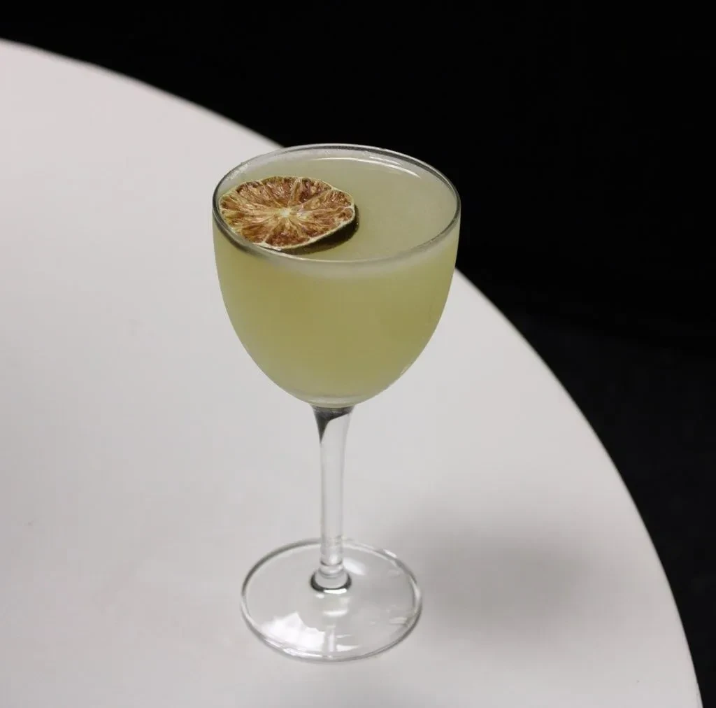 Opaque yellow-green cocktail with dried citrus garnish in a coupe glass.
