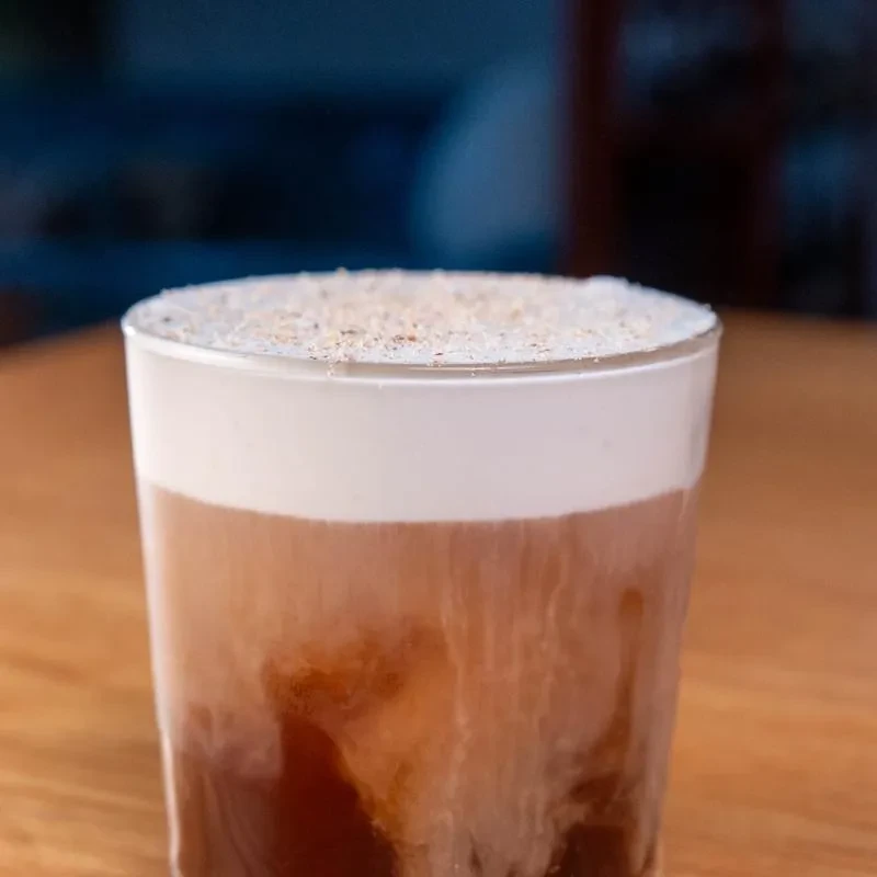 Iced layered coffee with white foam and brown spice.