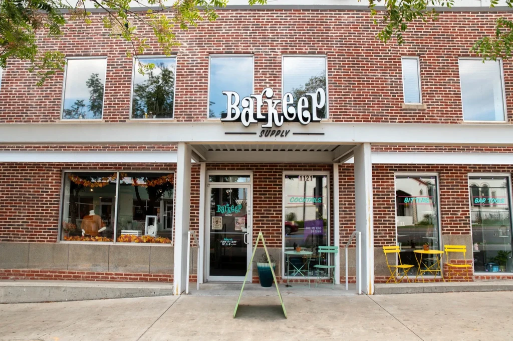 Two-story brick Barkeep Supply building with autumnal retail display and outdoor seating.