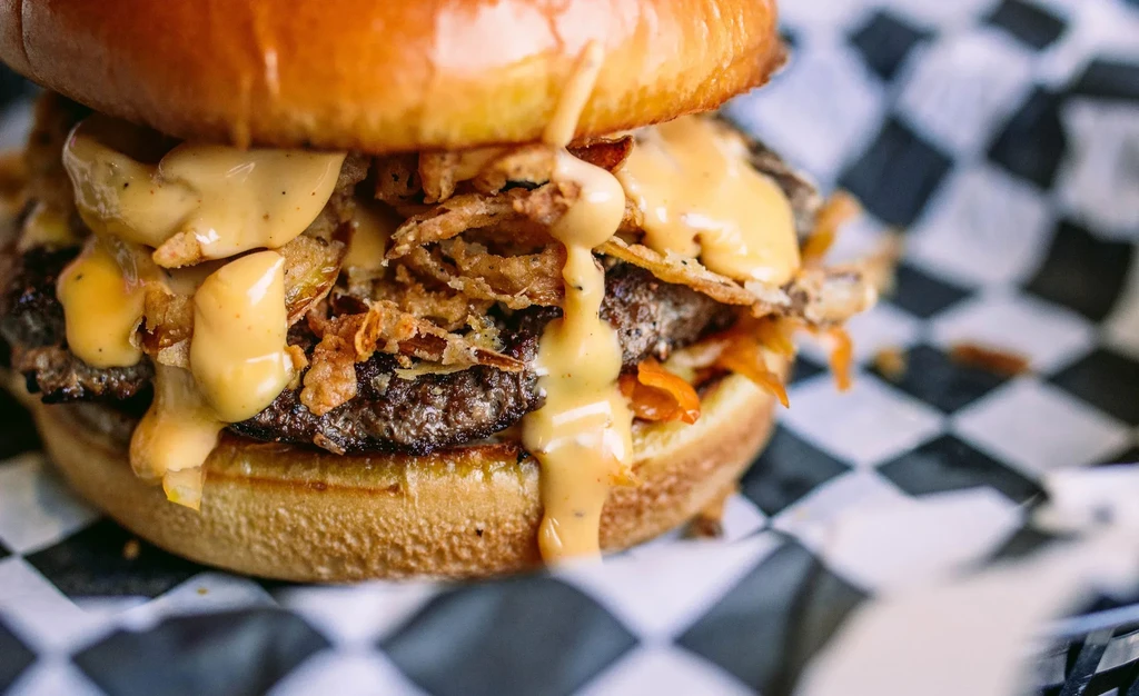 Close-up gourmet burger with sauce, crispy fried onions, and brioche bun.