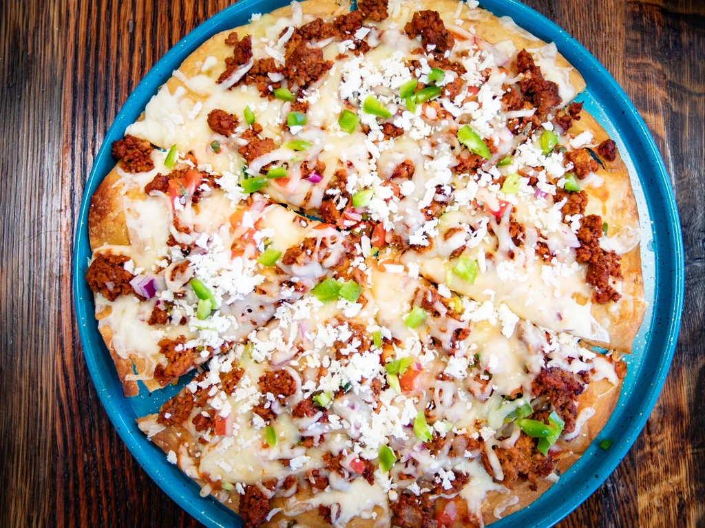 Overhead: savory flatbread with cheese, meat, peppers on a blue plate.