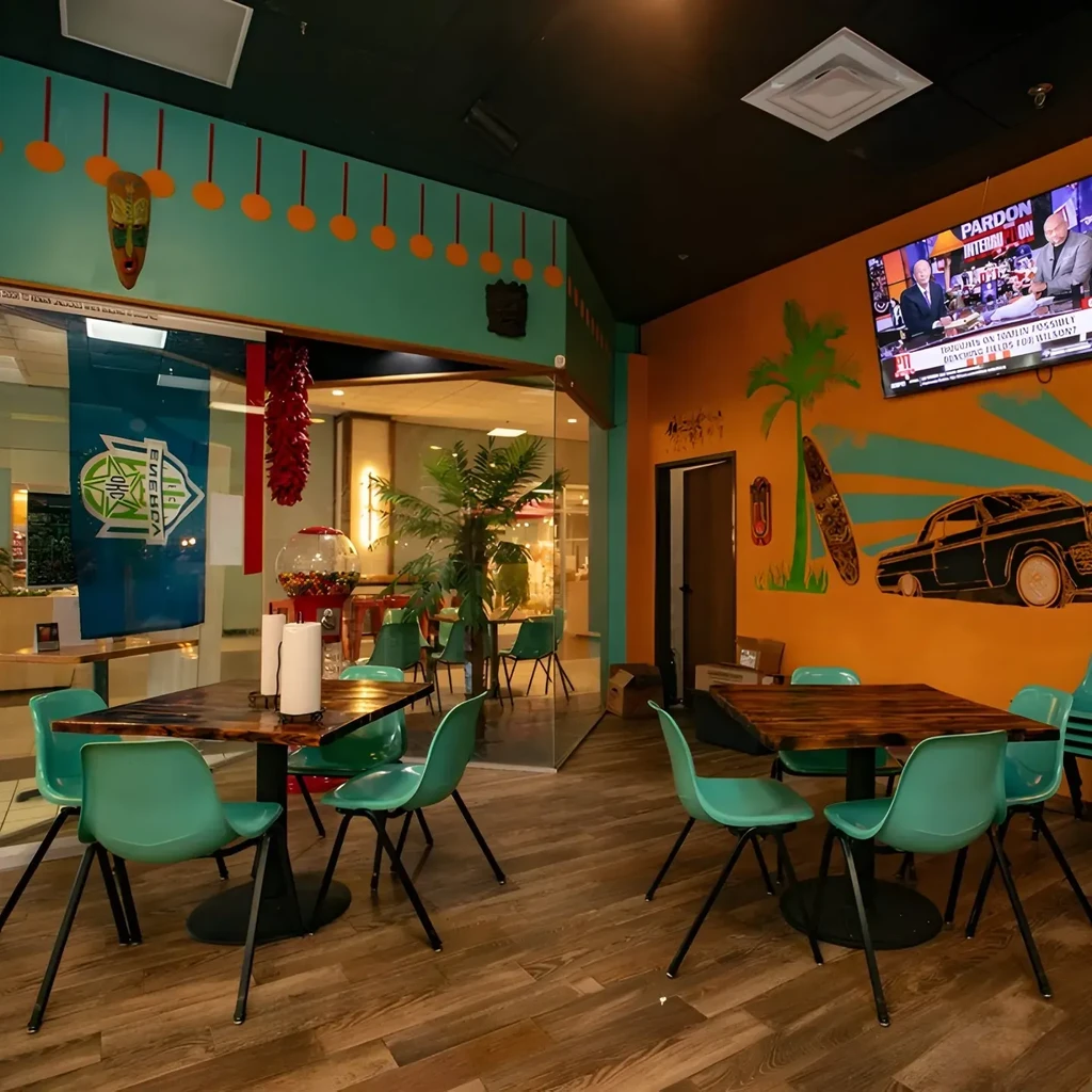 Restaurant dining area with teal chairs, orange mural, and TV.