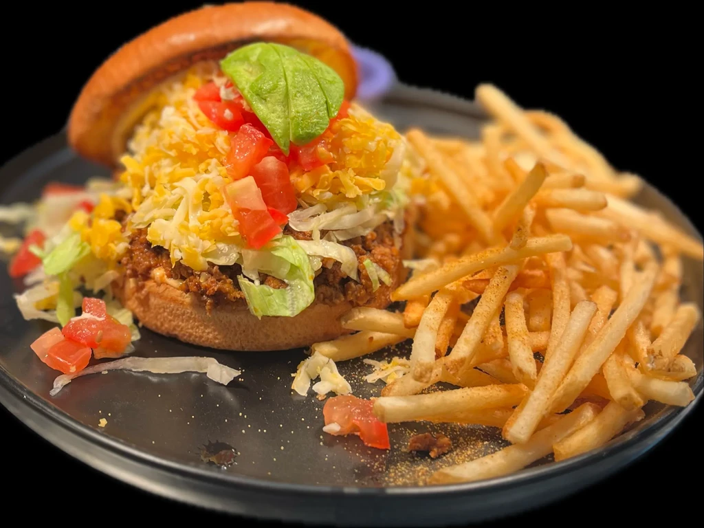 Open-faced sandwich with ground meat, cheese, avocado, and fries.