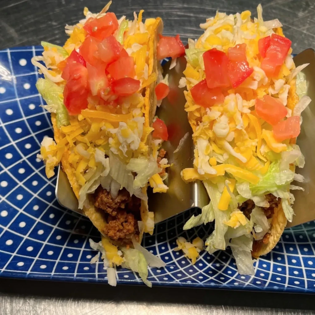 Two hard-shell tacos with meat, lettuce, cheese, tomatoes in a holder.