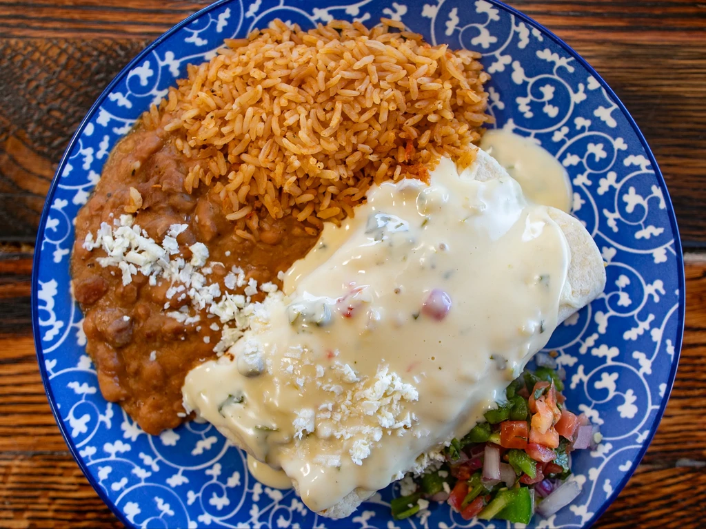 Top-down: Mexican rice, refried beans, cheese-covered enchilada, fresh pico de gallo.