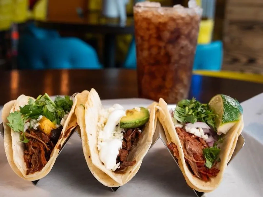Colorful soft-shell tacos with meat and diverse toppings in a metal holder.