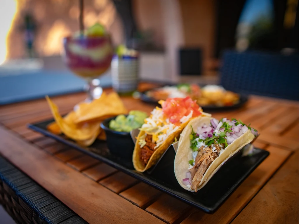 Two different tacos, guacamole, and chips on an outdoor table.