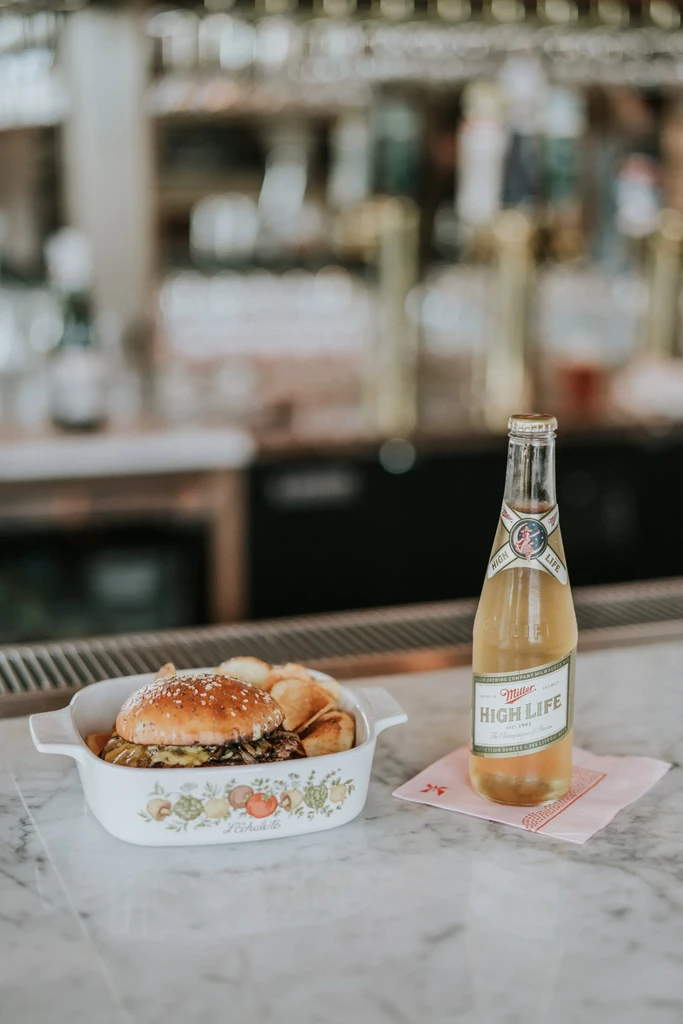 Sesame seed burger, chips, and beer bottle on marble counter.