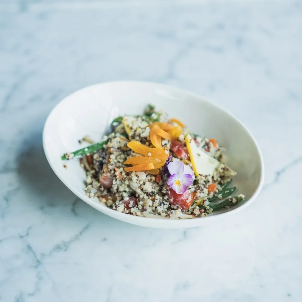 Vibrant quinoa salad with vegetables and edible flower in oval bowl.