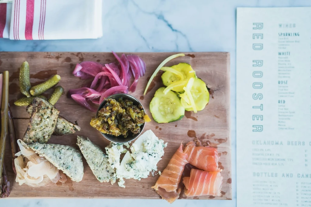 Overhead charcuterie board with salmon, cheese, pickles, pâté, and Red Rooster menu.
