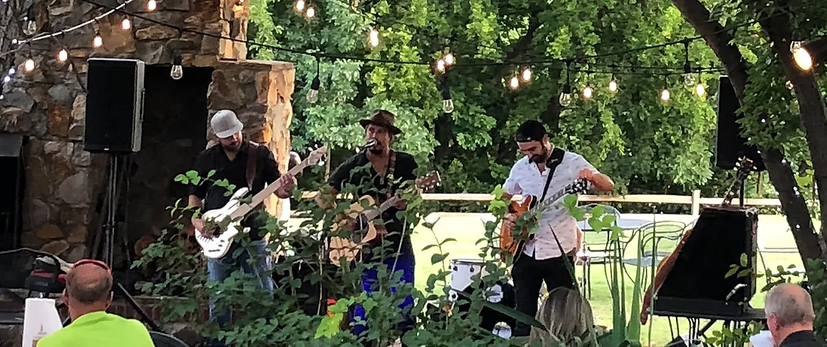 Band playing guitars on outdoor patio stage under string lights