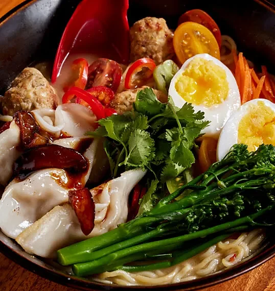 Ramen bowl with dumplings, soft egg, broccolini, tomato and cilantro