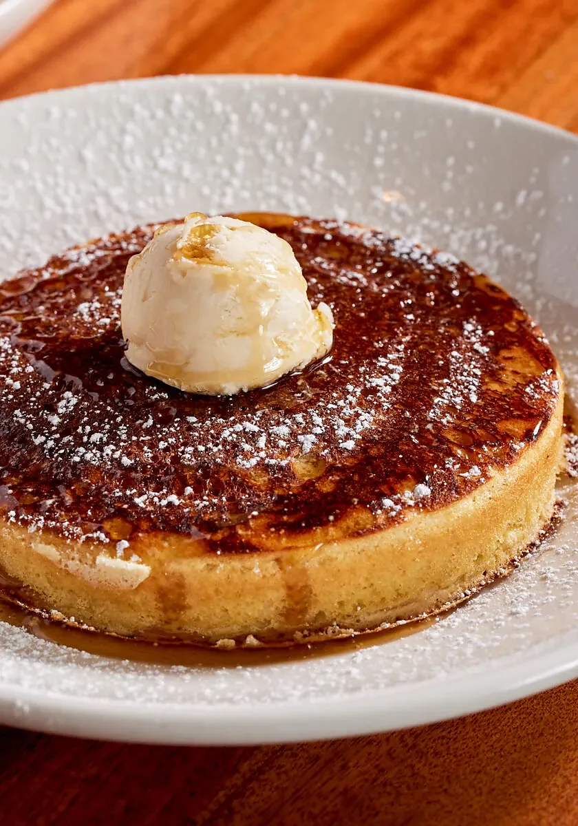 Thick pancake with powdered sugar, butter scoop and syrup on plate