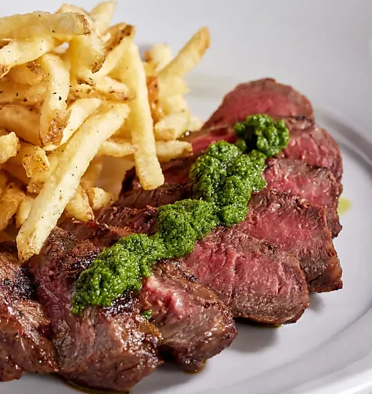 Sliced steak with chimichurri and hand-cut French fries on plate