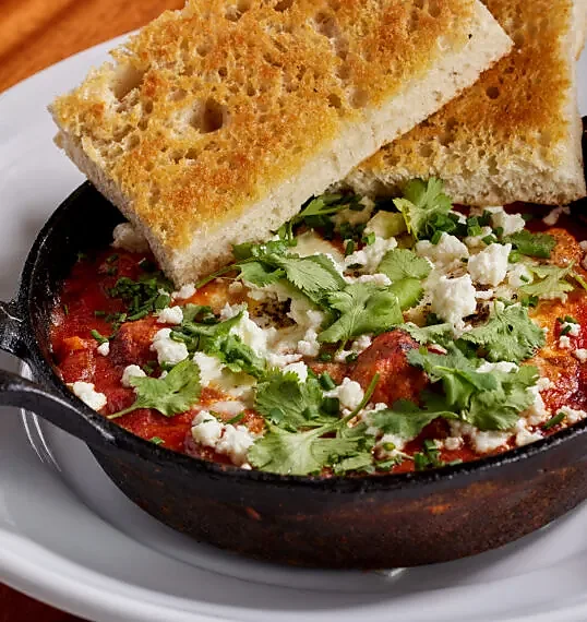 Cast iron skillet dish with tomato sauce, feta, cilantro and focaccia