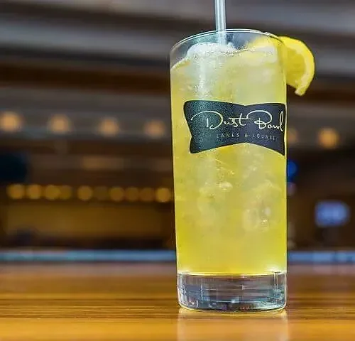 Yellow cocktail with lemon wedge in Dust Bowl branded glass on bar