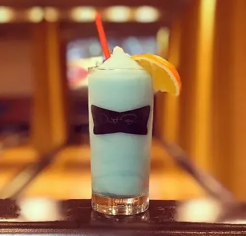 Light blue frozen cocktail with orange slice, bowling lanes in background