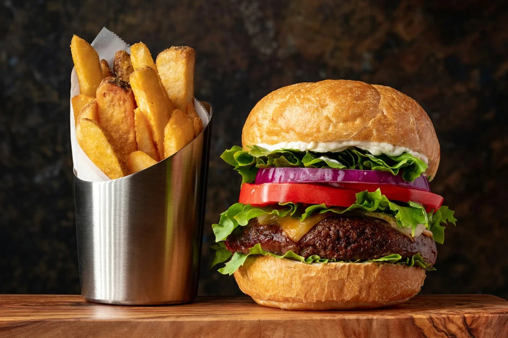 Close-up of gourmet cheeseburger, crispy fries, white sauce on wood.