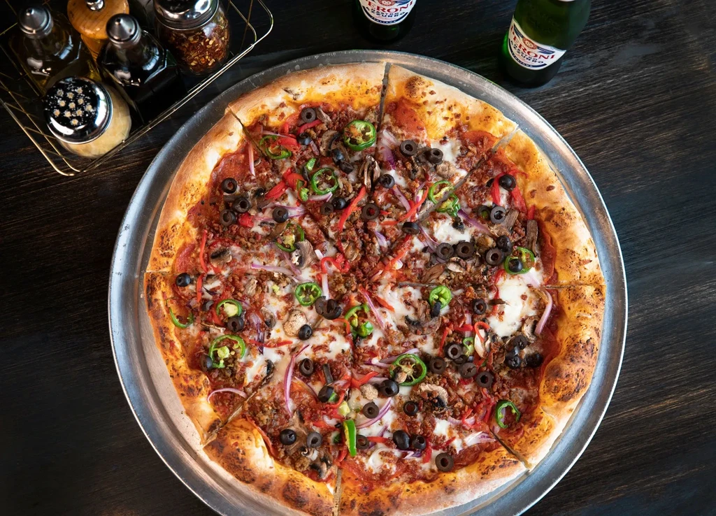 Overhead: Sliced, multi-topping pizza on a pan with beer and condiments.