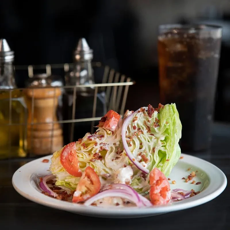 Wedge salad with creamy dressing, bacon, tomato, and red onion.