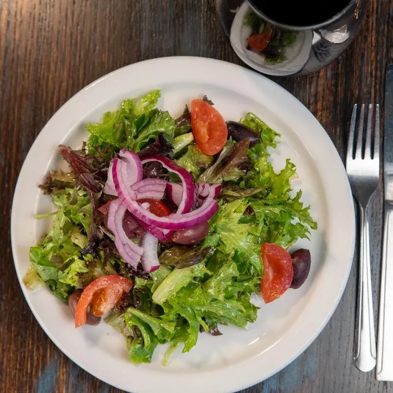 Overhead shot of fresh salad with tomato, olives, onion, fork, wine.