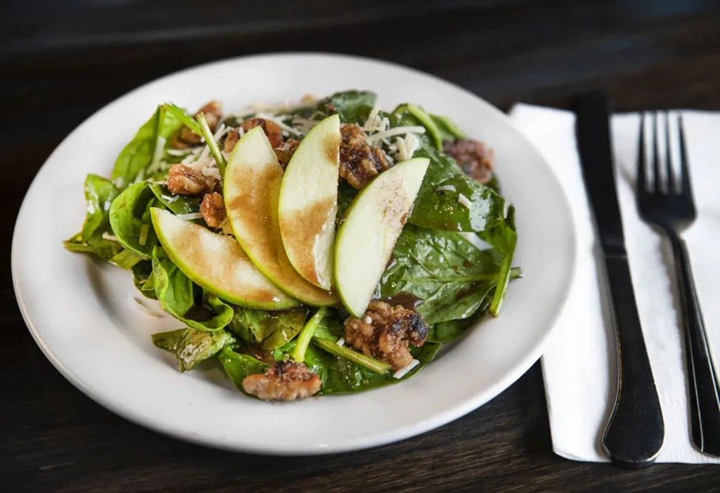 Overhead salad with spinach, apple, candied nuts, cheese, and dressing.