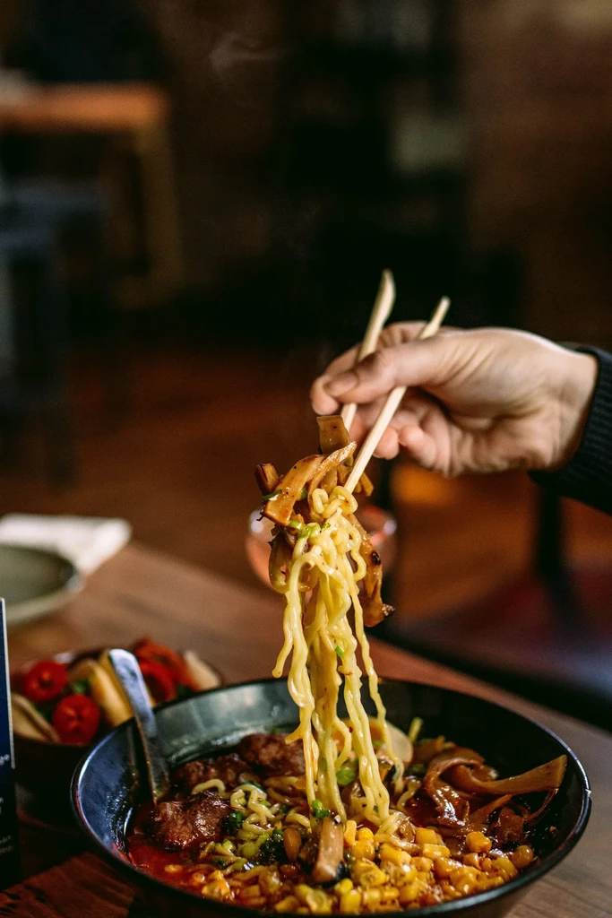 Close-up of steaming ramen bowl, chopsticks lifting noodles and toppings.