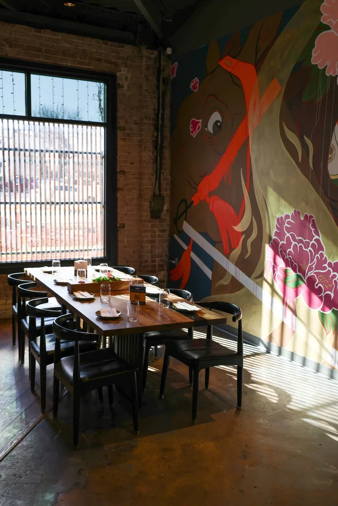 Restaurant interior: long table, black chairs, bright mural, exposed brick.
