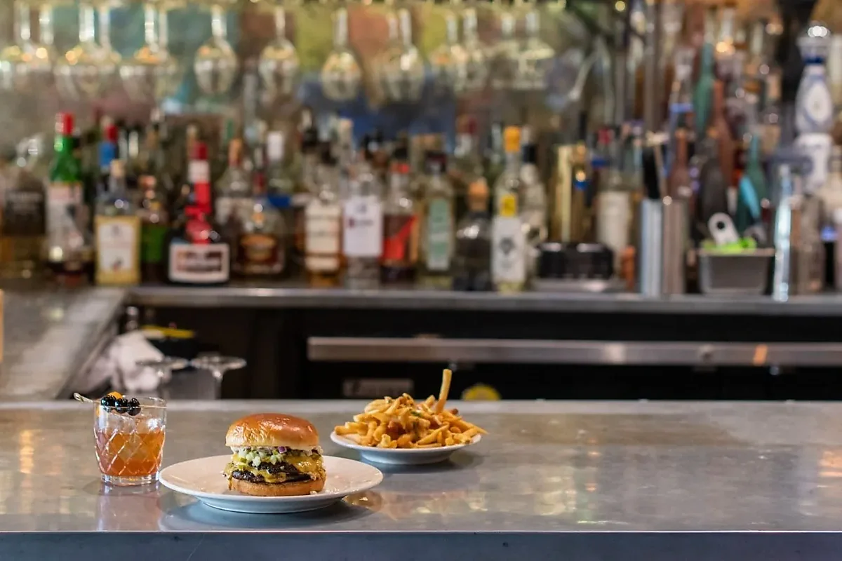 Burger, fries and old fashioned on metal bar top