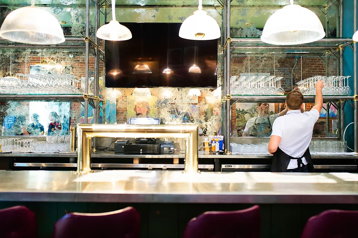 Bartender stocking glassware behind mirrored back bar with pendant lights