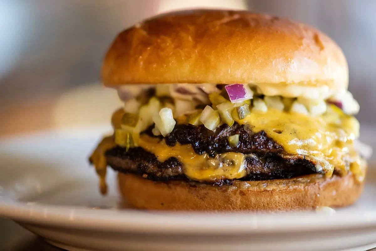 Close-up of double cheeseburger with pickles and diced onion on bun