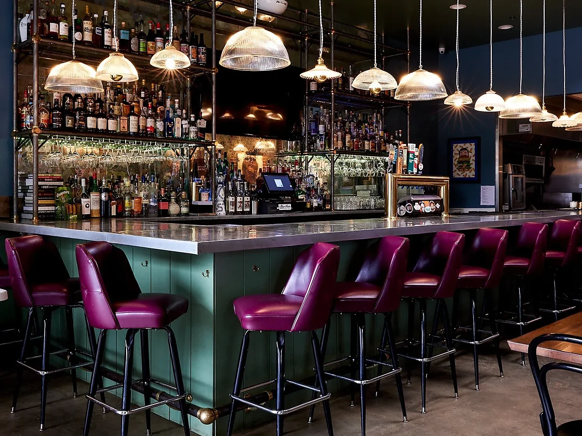 Green bar with purple stools, liquor shelves and pendant lighting