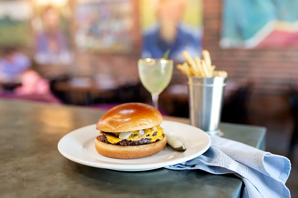 Cheeseburger on white plate with pickle and metal cup of fries