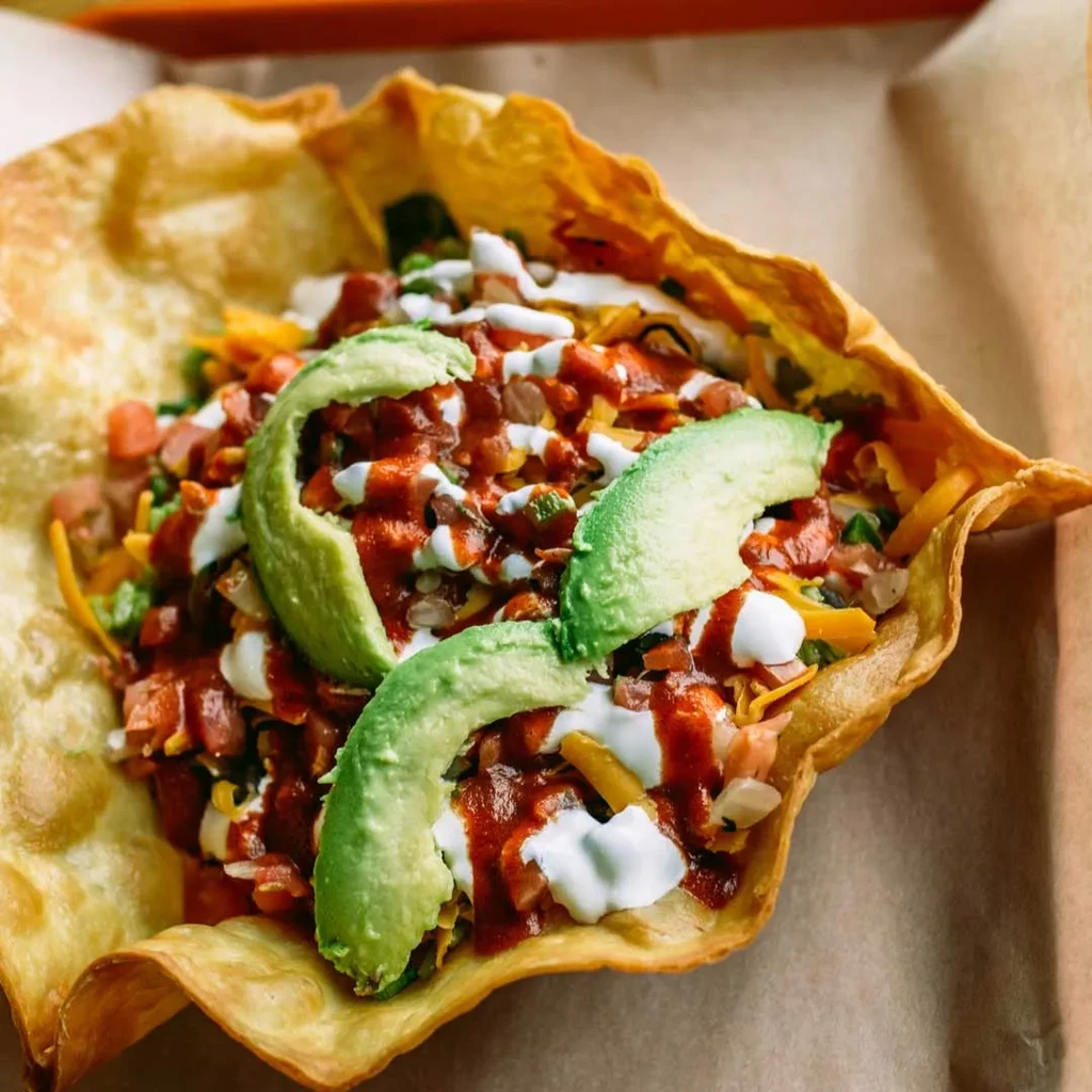 Colorful taco salad in a crispy fried tortilla bowl with avocado.