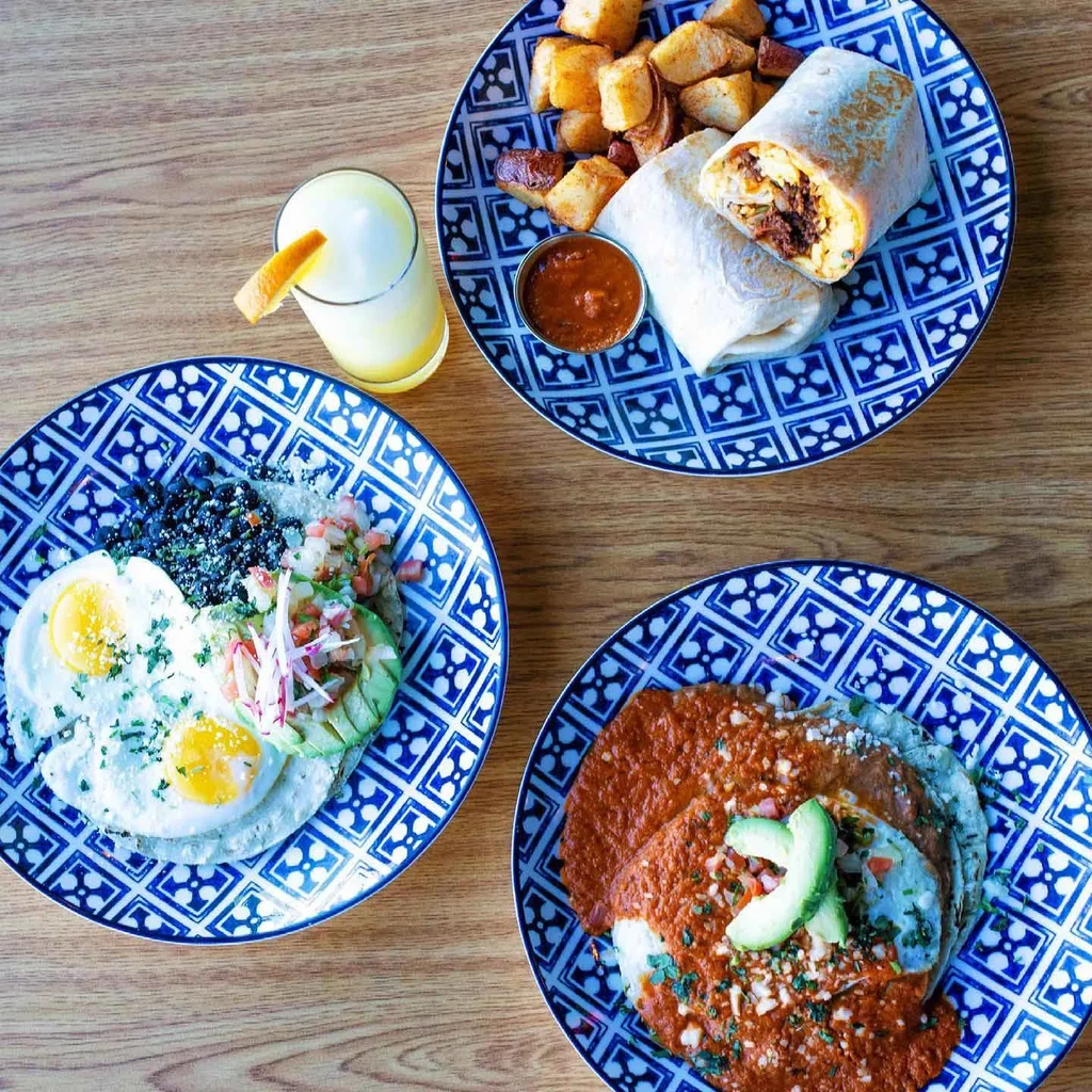 Overhead view of three Mexican-style breakfast dishes and orange juice on wood.