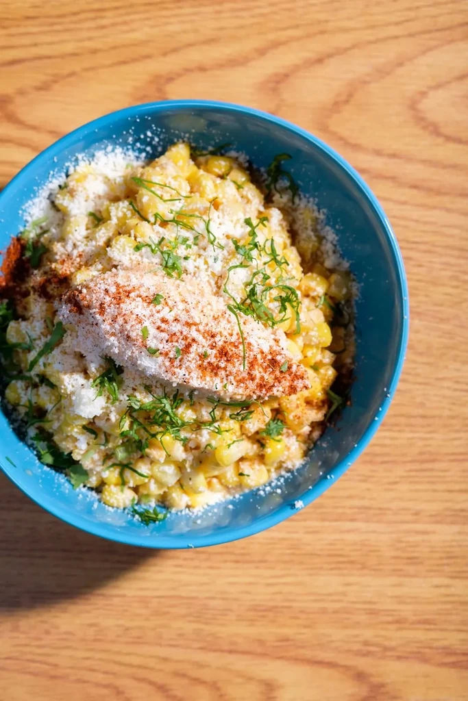 Teal bowl of corn salad topped with cheese, cilantro, and chili.