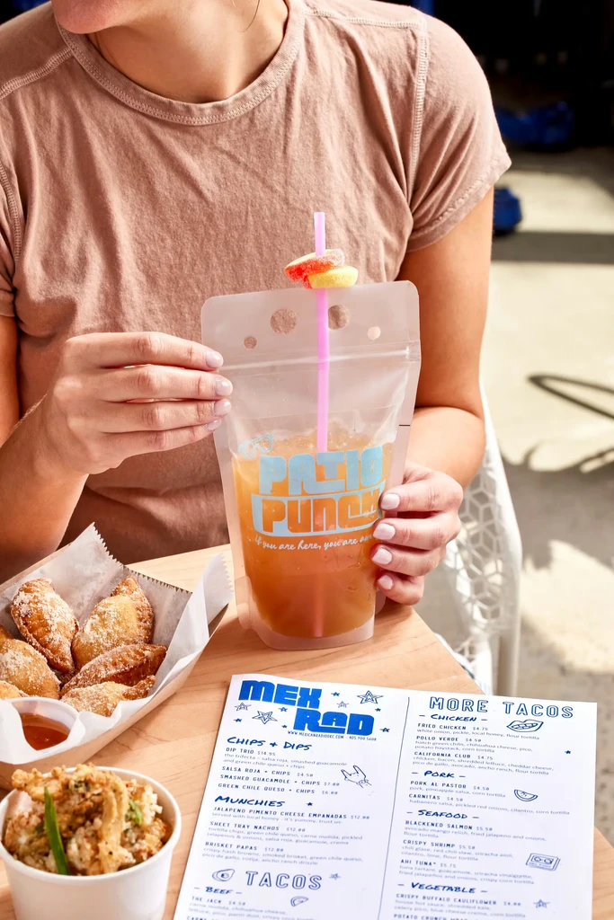 Hands holding "Patio Punch" drink with gummies, empanadas, and a menu.