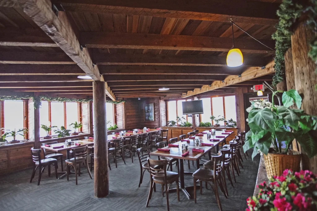 Spacious, rustic restaurant interior with wooden tables, beams, and windows.