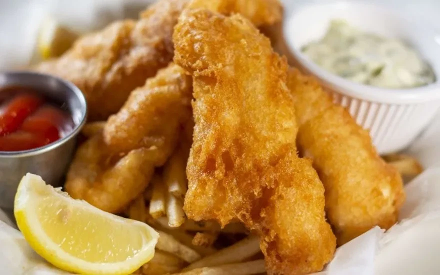 Fish and chips with lemon, ketchup, and tartar sauce in a basket.
