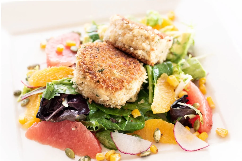 Two breaded patties on a colorful salad with citrus and mixed greens.