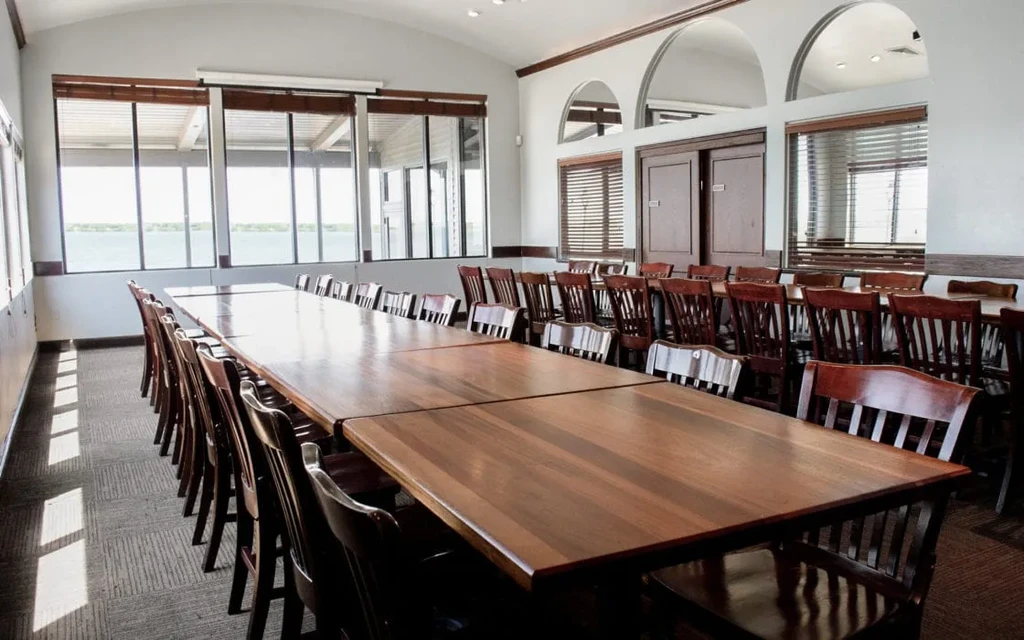 Bright private dining room with long table, chairs, and water view.